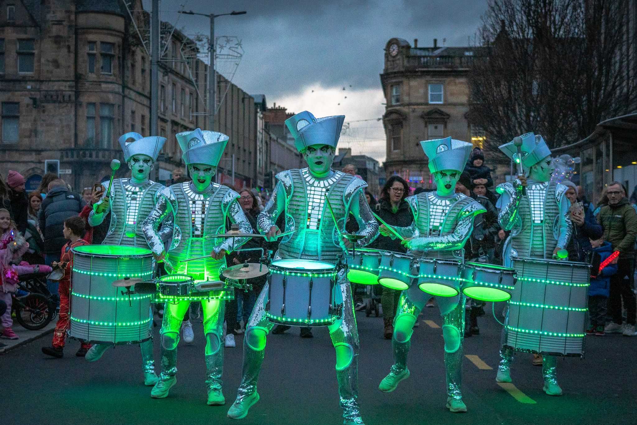 Performers at Paisley Halloween Festival lit by green LED lights as they drum