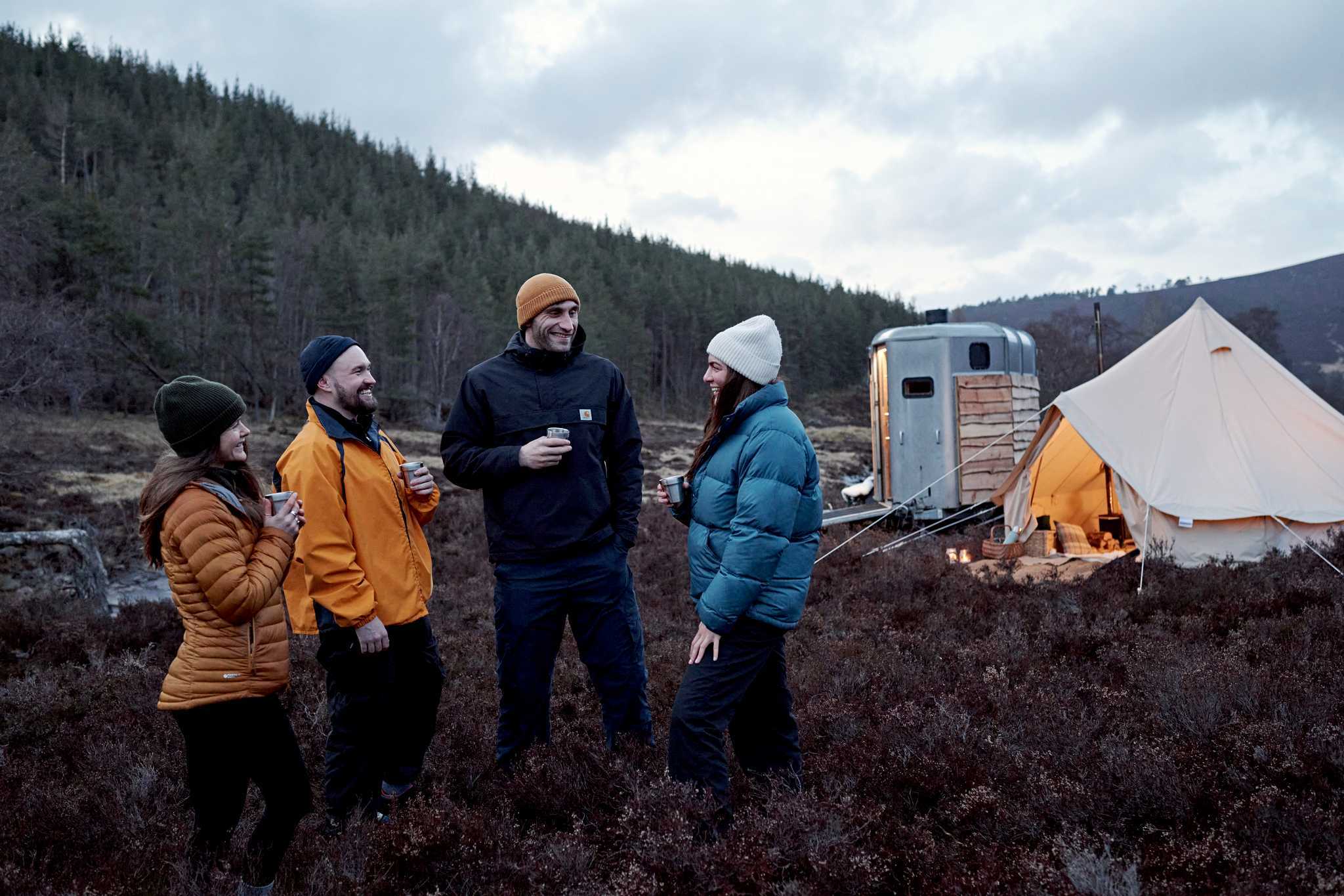 two couples chatting cheerfully beside a camping tent and trailer unit