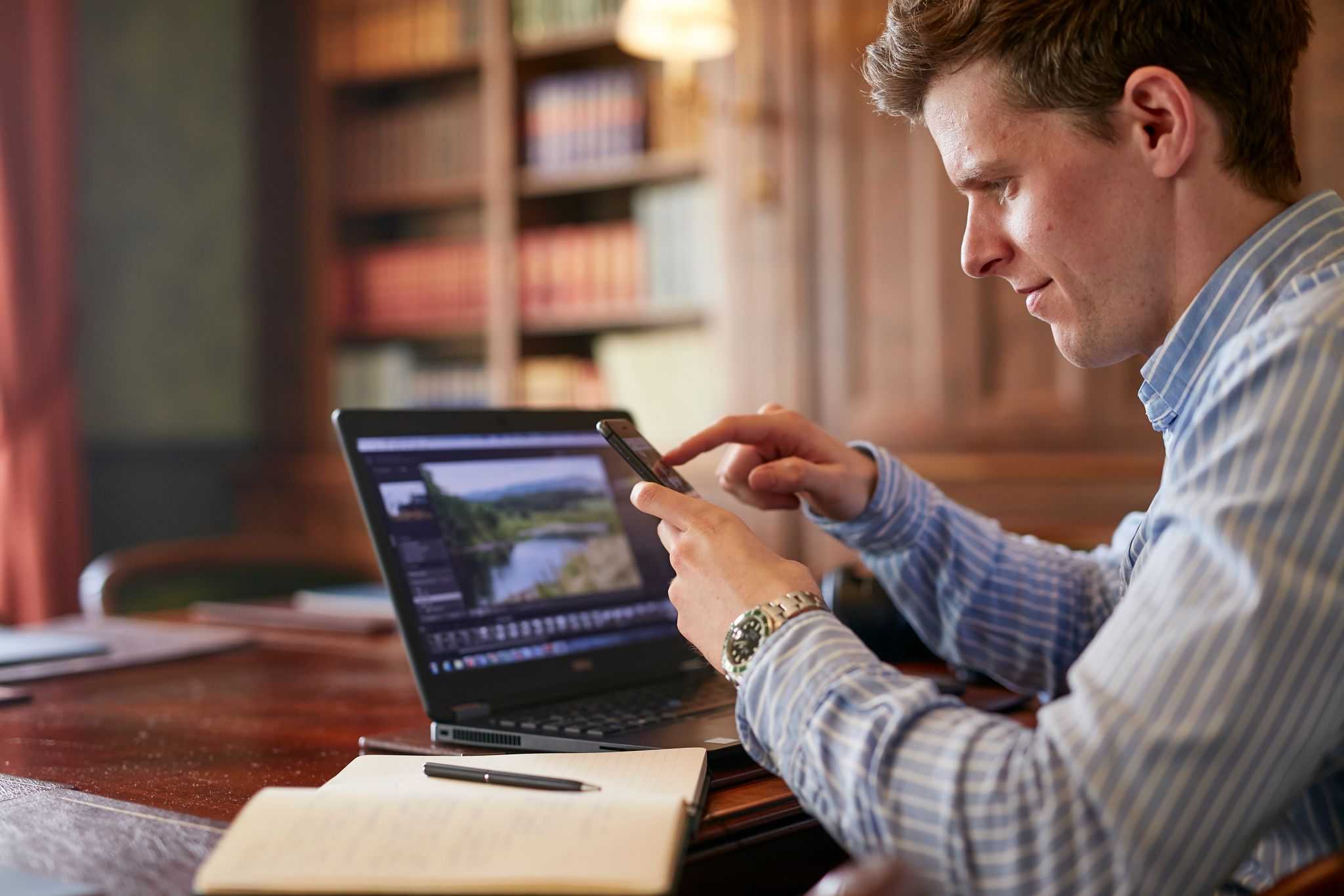 Man sitting at laptop looking at his phone.