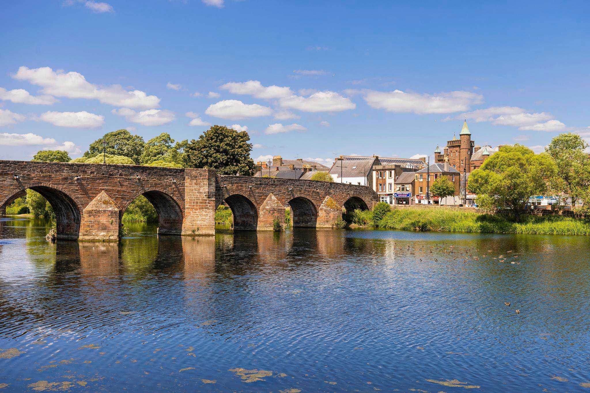 A beautiful stone bridge with arches crossing a on a sunny day.
