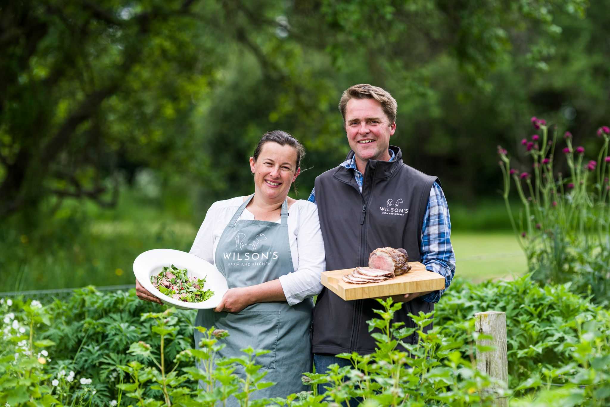 A couple stand display plates of food while standing in a garden