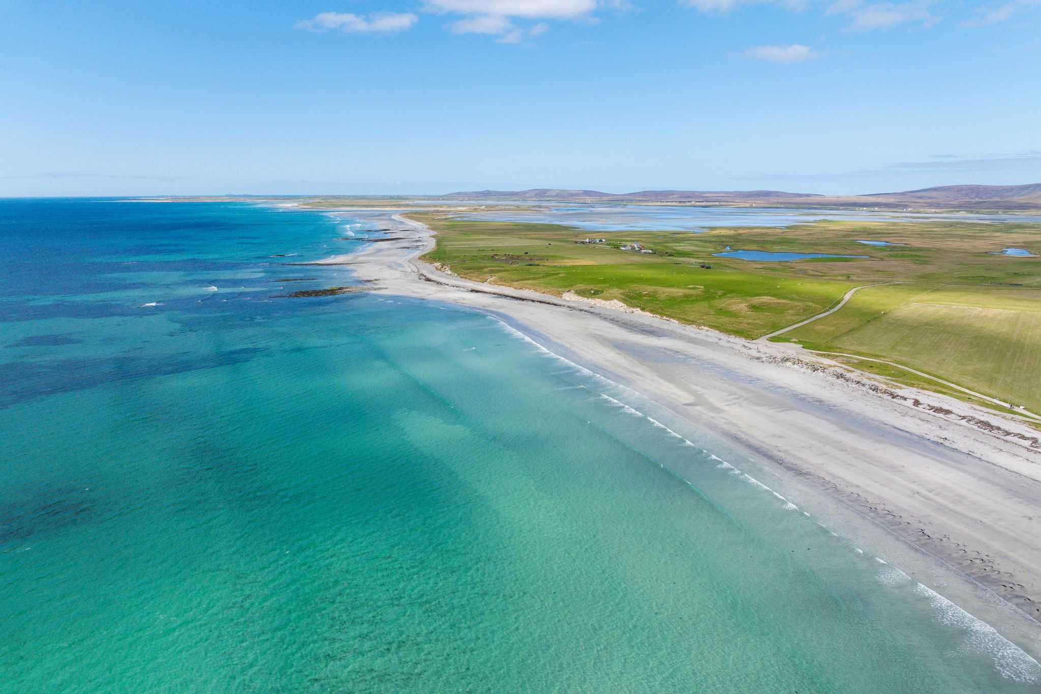 Turquoise coloured sea washes onto a long quiet beach on a sunny day.