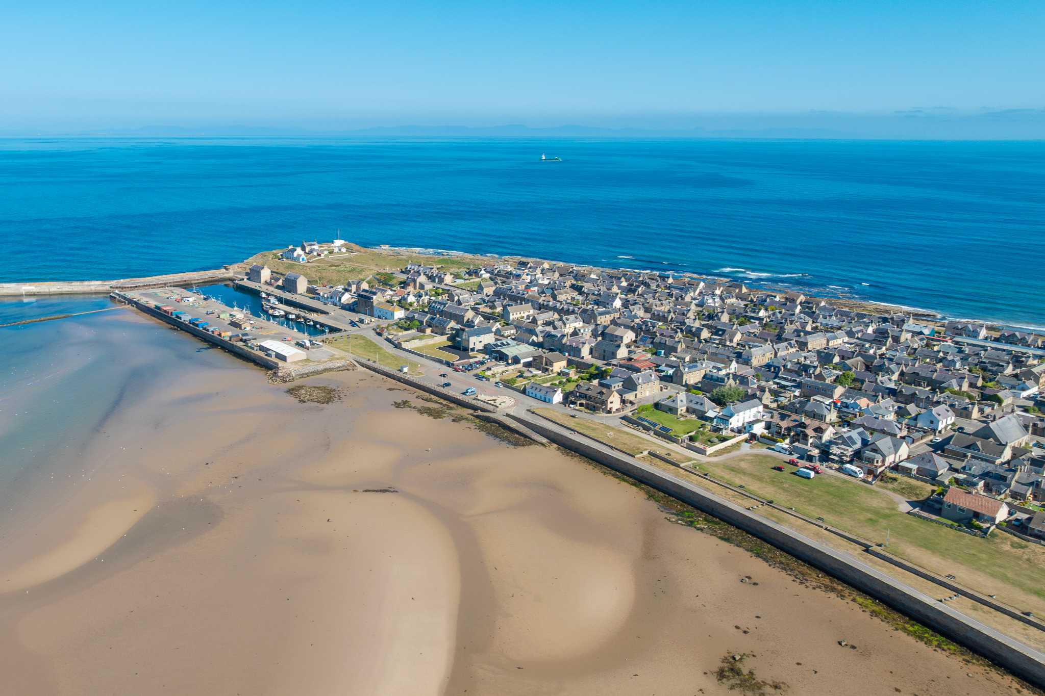 An ariel shot of a a sandy peninsula with buildings on a clear day. The sea and sky are a bright blue.