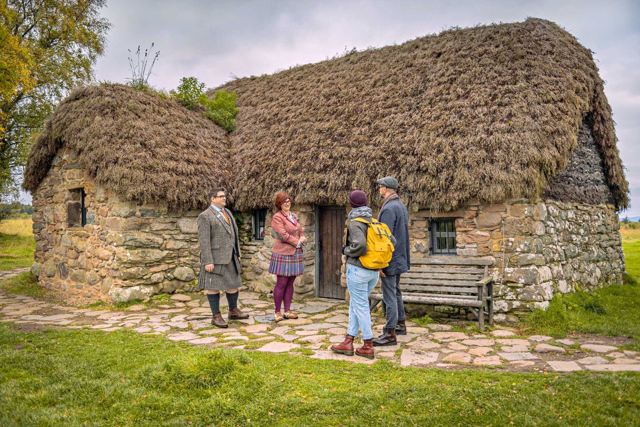 Two members of staff in engage with visitors outside a thatched cottage style building.