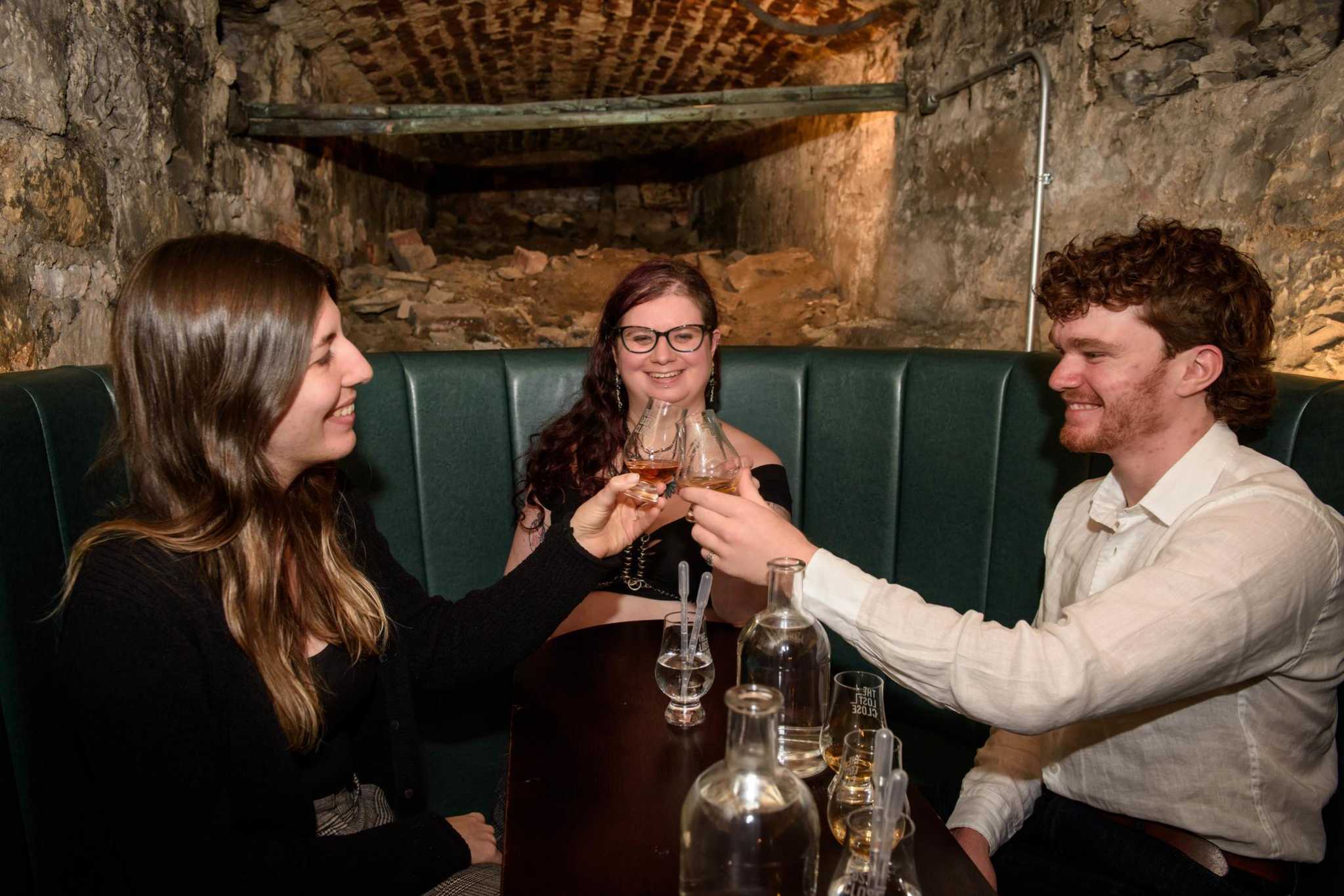 A group seated at a table raise their whisky glasses to say cheers.
