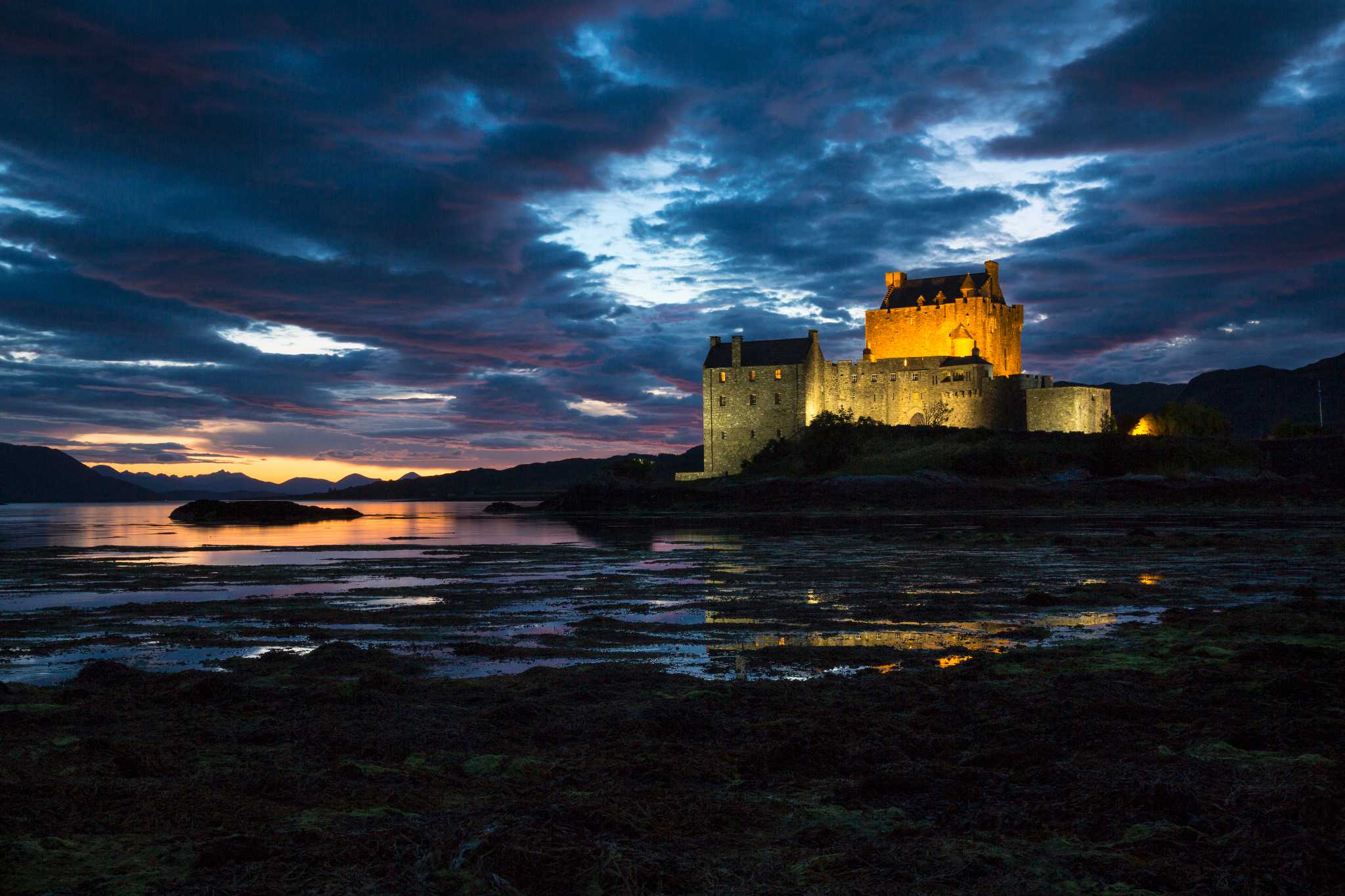 Castle lit up as the sun sets in over hills and loch in background