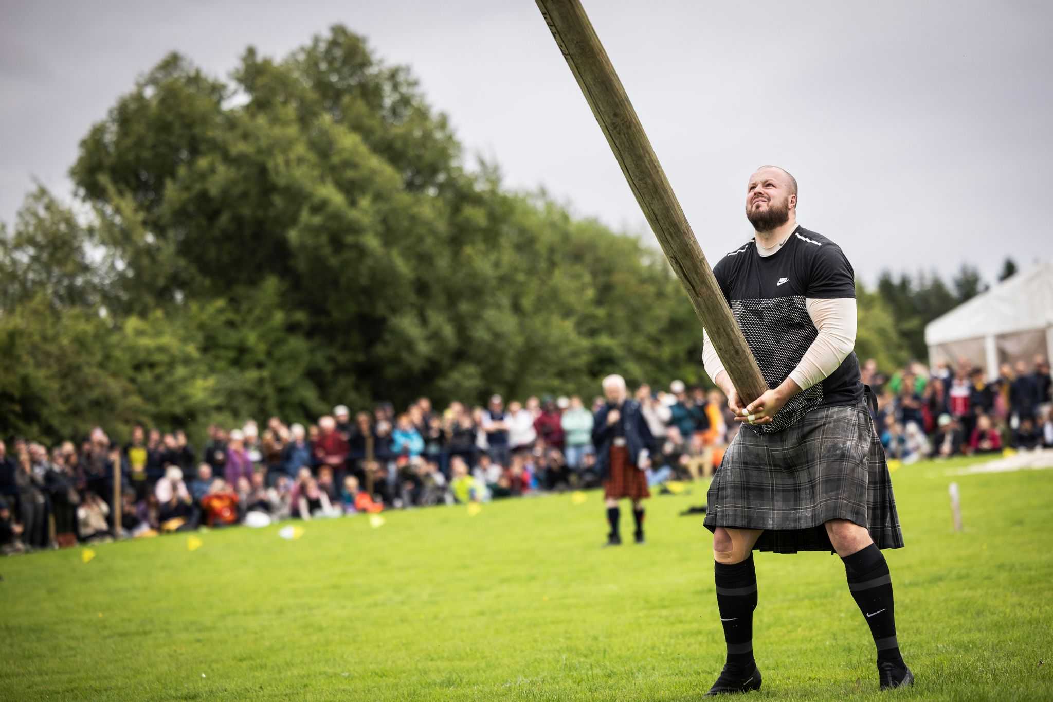 A kilted man tossing a large caber in front of a crowd