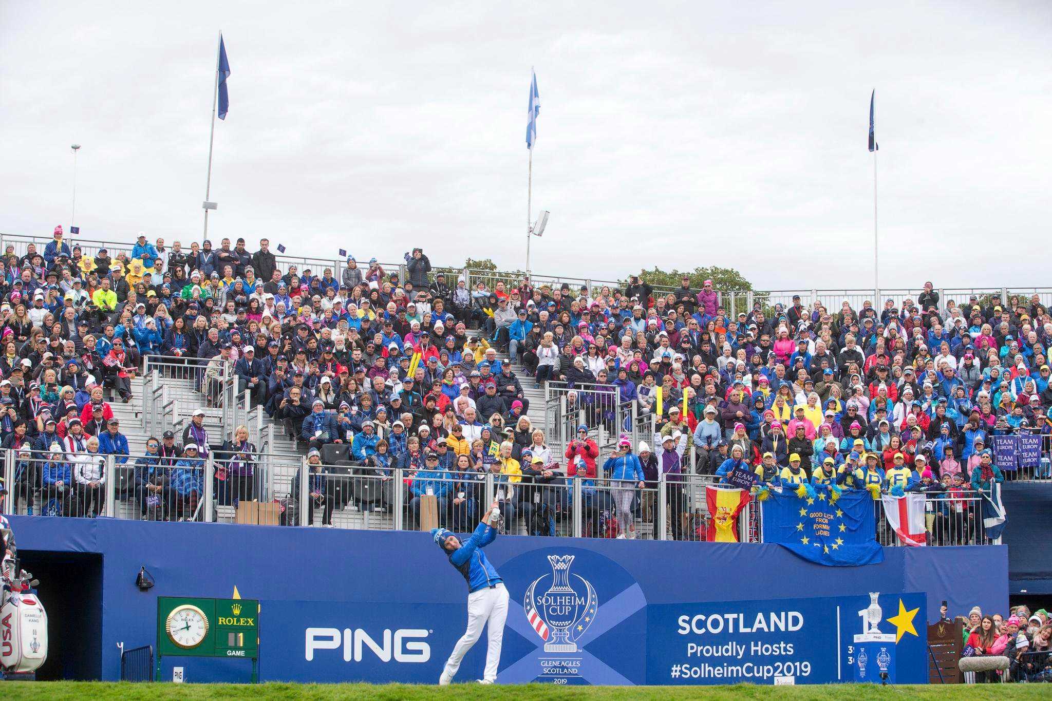 A golfer takes a swing as a large crowd looks on from the stands