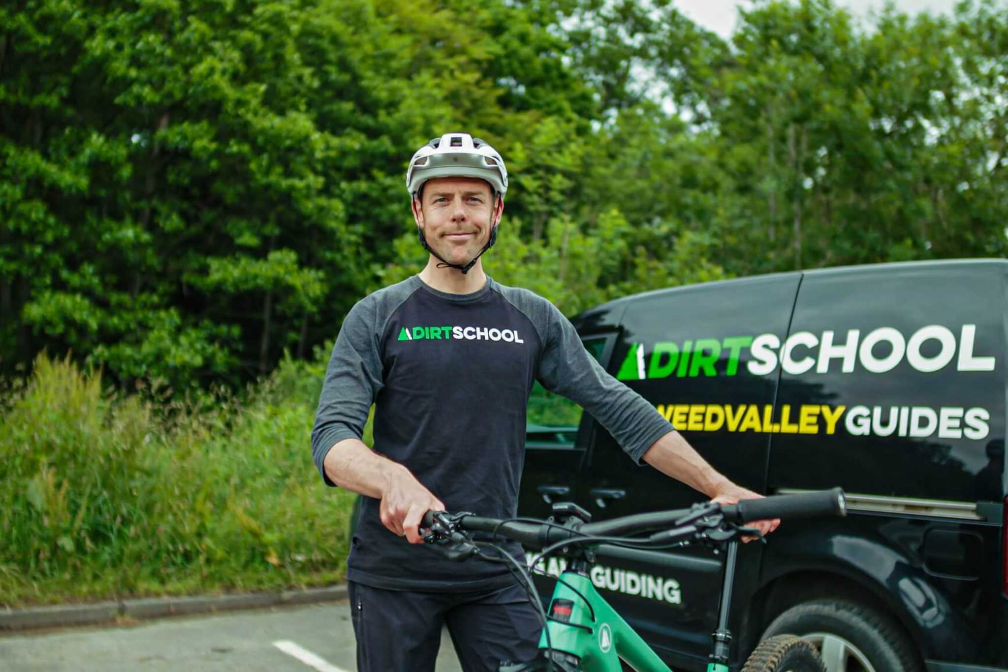 A man with a mountain bike and cycling helmet stands beside a van