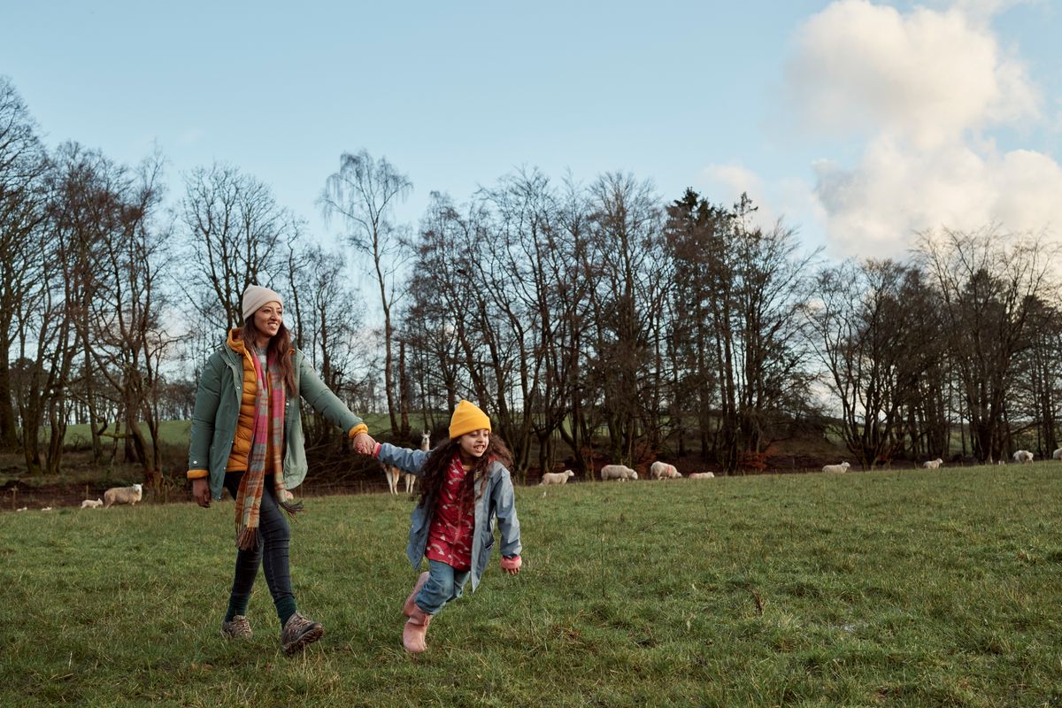 A mother and daughter walking in a field with sheep in background