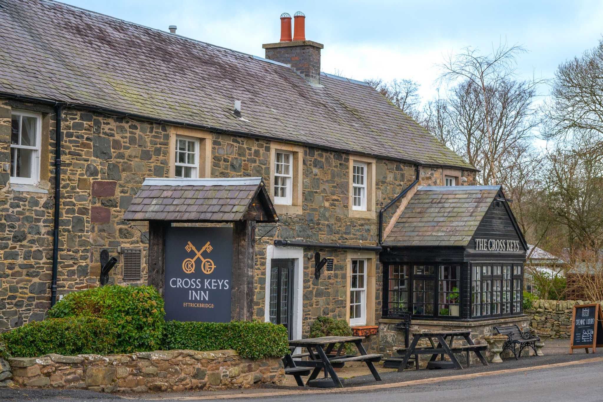 A countryside Inn with exterior dining tables and signage surrounded by stone wall.