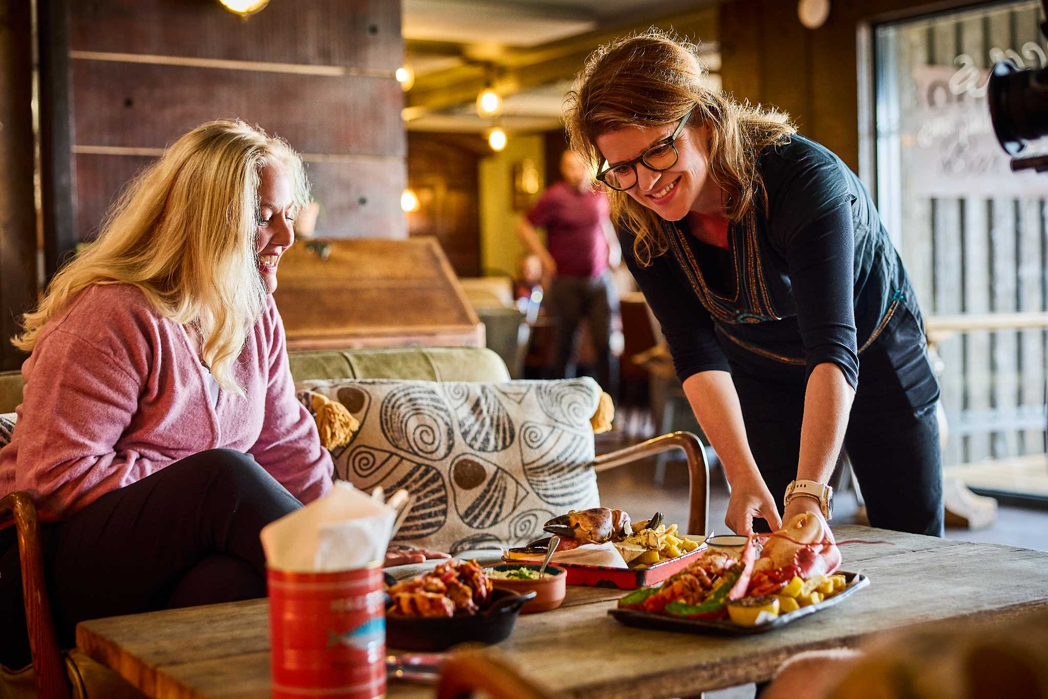 A lady is served plates of colourful looking food in a bar setting.