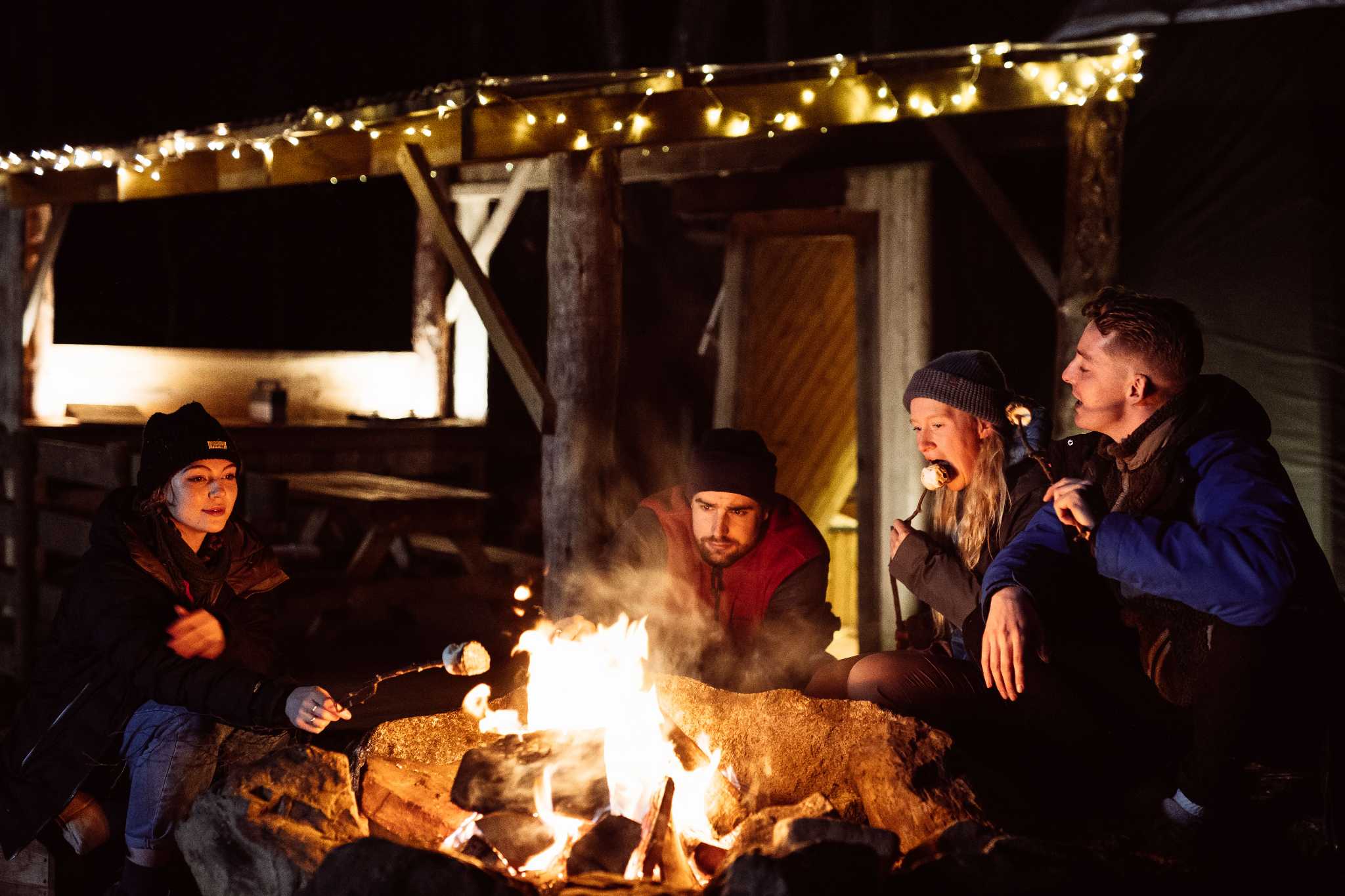 Four people sitting around a campfire toasting marshmallows