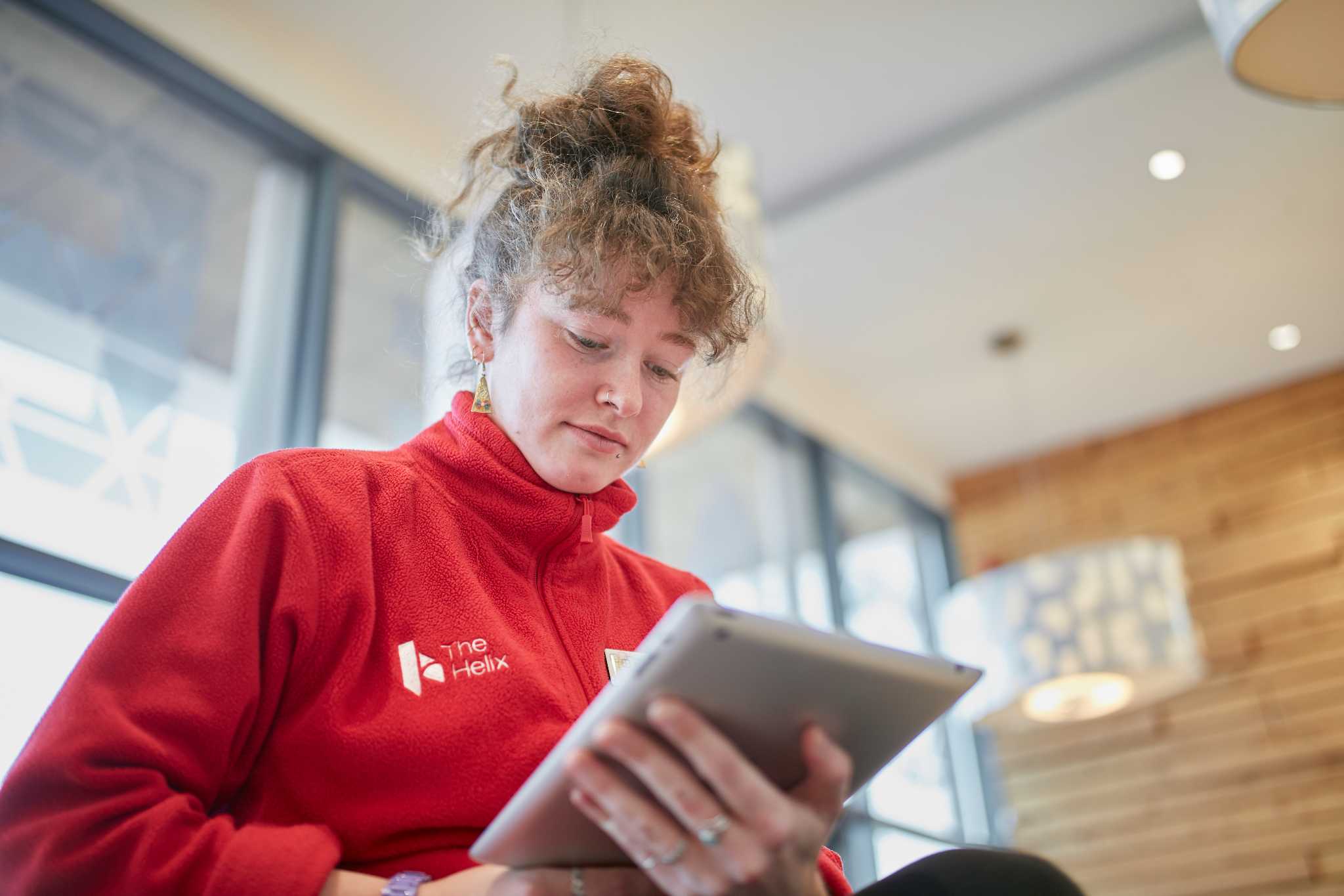 A lady in a company branded red fleece is concentrating on the tablet device she is using.