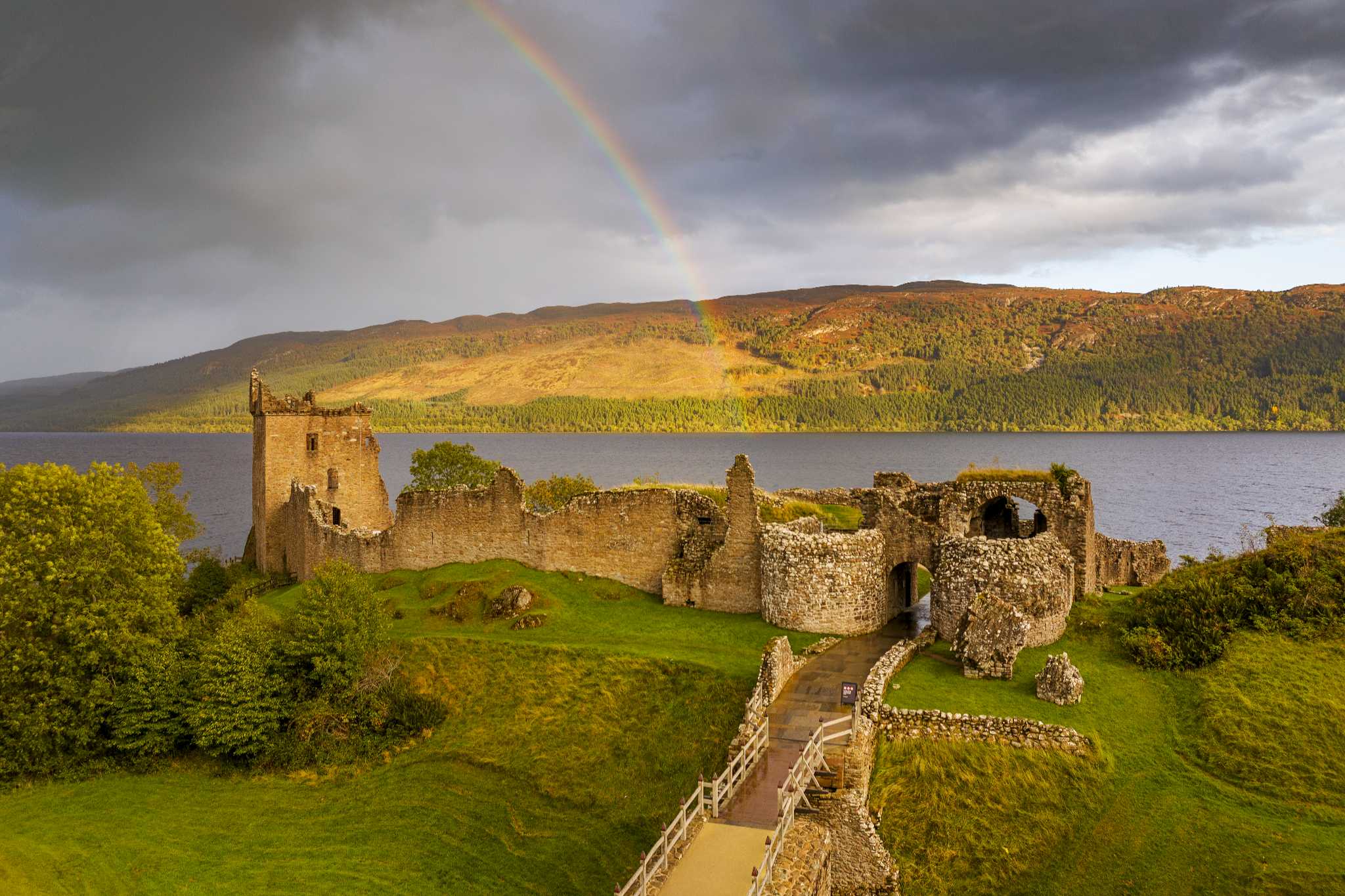 Looking at Urquhart Castle on the banks of Loch Ness with a rainbow in the sky.