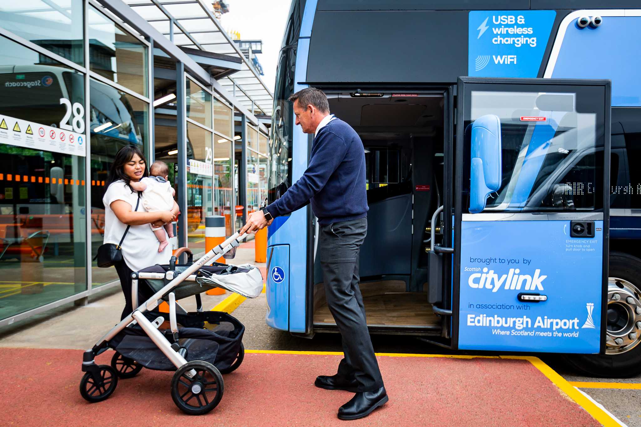 A bus driver assists a lady with a small child getting on a bus, by taking her buggy.